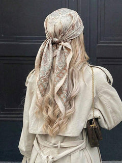 Vista trasera de una mujer con cabello rubio usando un pañuelo estampado en tonos beige atado en la cabeza.