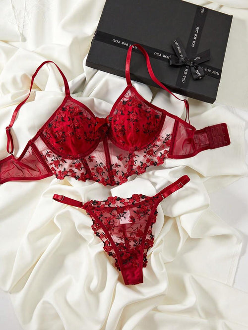 Conjunto de lencería rojo con bordado floral y tanga a juego sobre una tela de seda blanca.