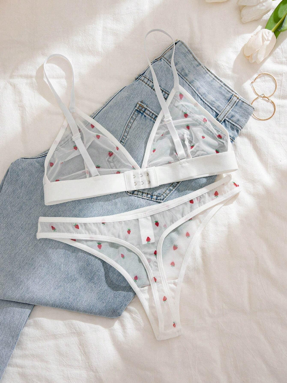 Set de lencería blanco con estampado de fresas sobre jeans - vista frontal.