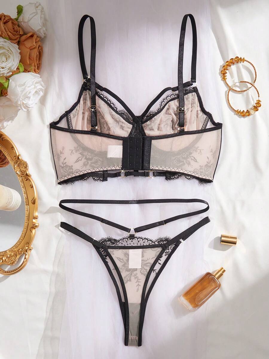 Conjunto de lencería de dos piezas con bordado floral negro sobre base nude, dispuesto sobre una tela blanca.