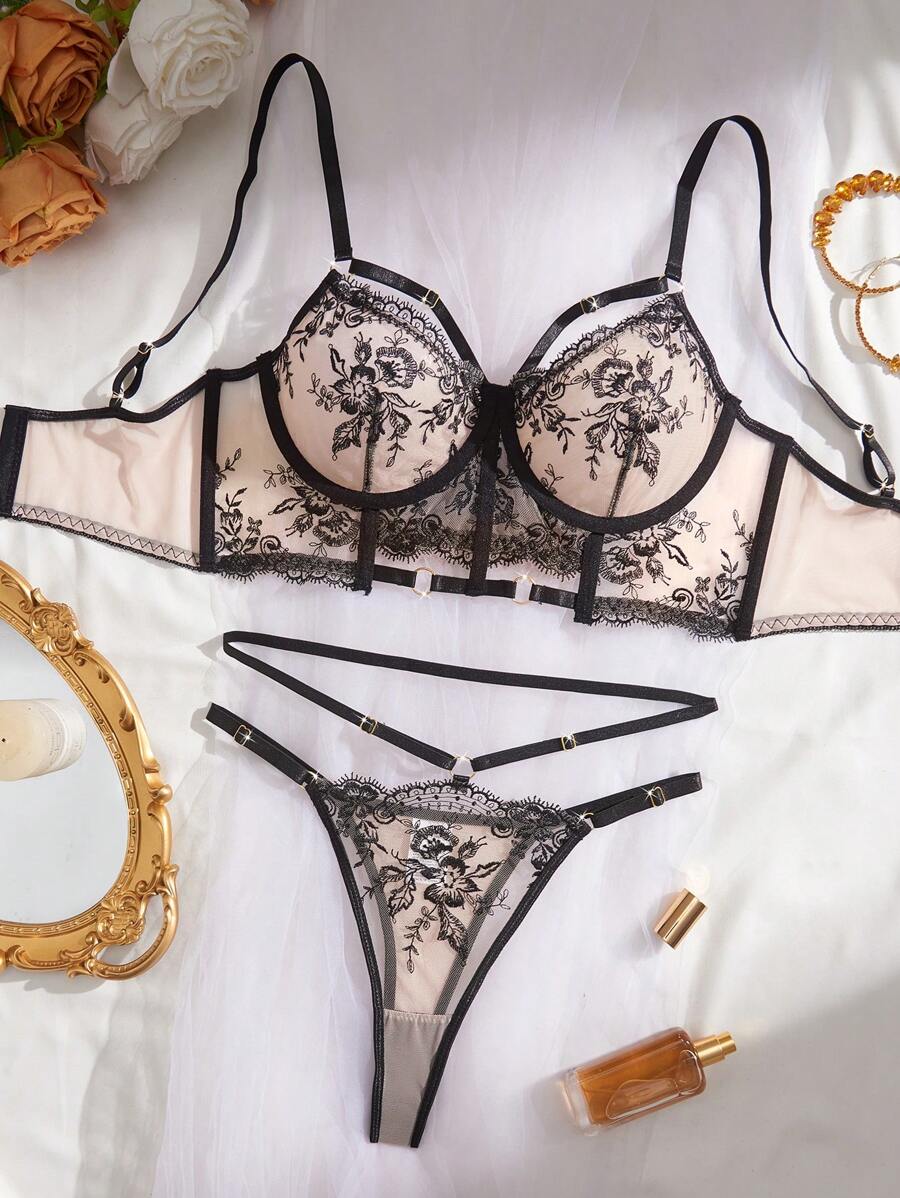 Conjunto de lencería de dos piezas con bordado floral negro sobre base nude, dispuesto sobre una tela blanca.