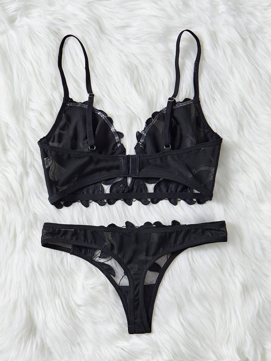 Conjunto de lencería negro de dos piezas con bordado floral sobre un fondo de peluche blanco.