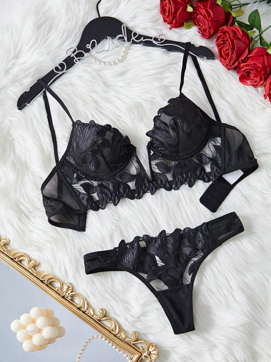 Conjunto de lencería negro de dos piezas con bordado floral sobre un fondo de peluche blanco.