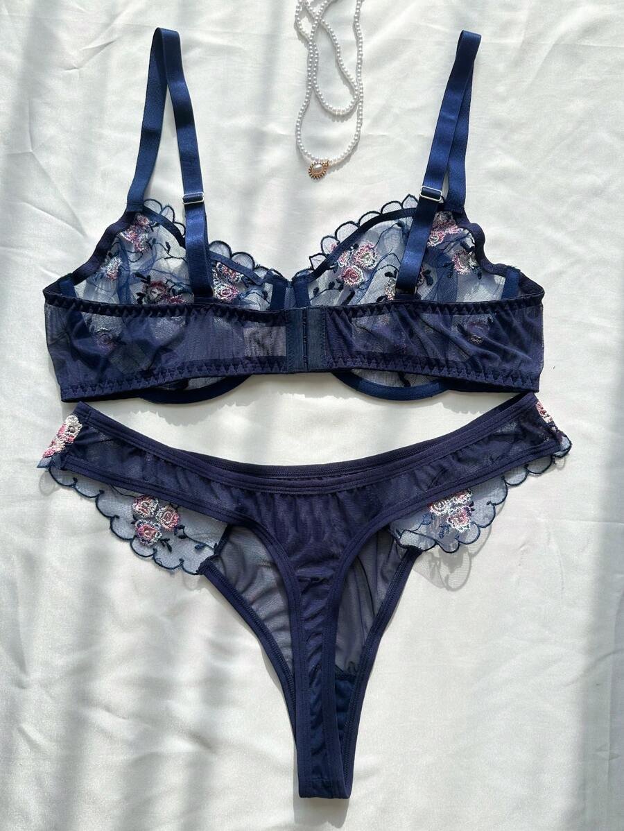 Set de lencería azul con bordado floral transparente sobre superficie blanca.