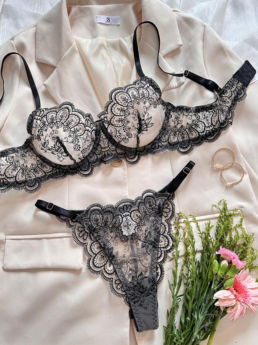 Conjunto de lencería de encaje negro con bordado floral visto desde arriba sobre una chaqueta color crema.