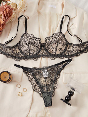 Conjunto de lencería de encaje negro con bordado floral visto desde arriba sobre una chaqueta color crema.