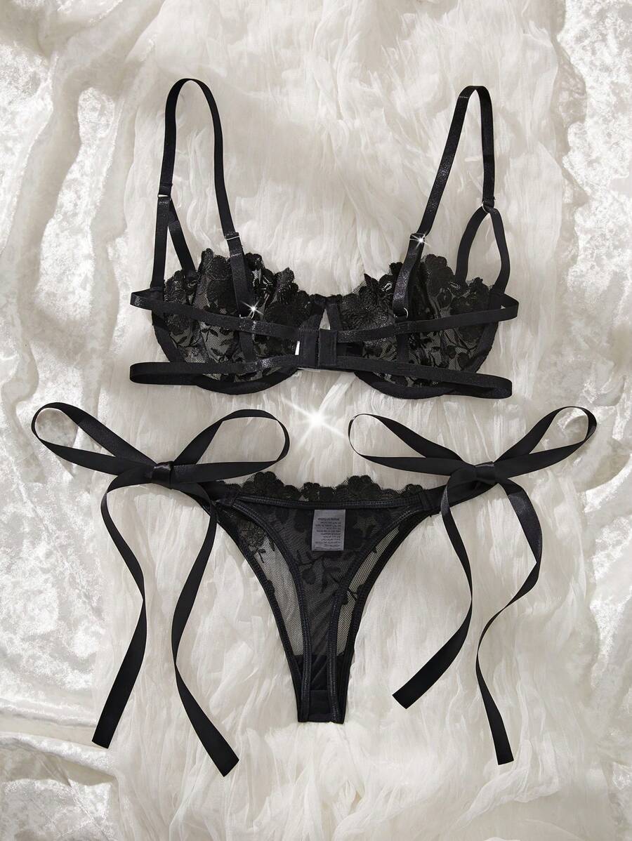 Conjunto de lencería de encaje floral negro sobre un fondo de tela blanca.