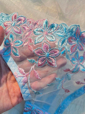 Panty tipo tanga a juego con bordado floral y bordes ondulados.