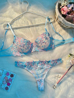 Conjunto de lencería con bordado floral en tonos celeste y rosa sobre un fondo de seda.