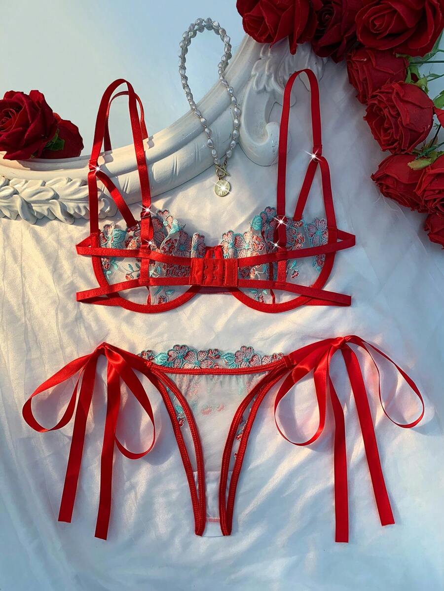 Conjunto de lencería rojo con bordado floral turquesa sobre una superficie blanca.