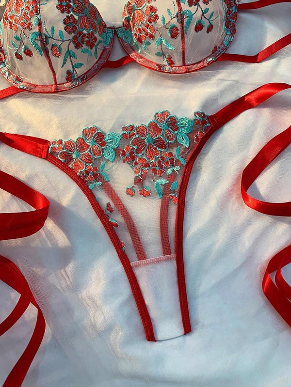 Vista detallada de la tanga de lencería con malla transparente y bordado floral en rojo y turquesa.