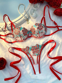 Conjunto de lencería rojo con bordado floral turquesa sobre una superficie blanca.