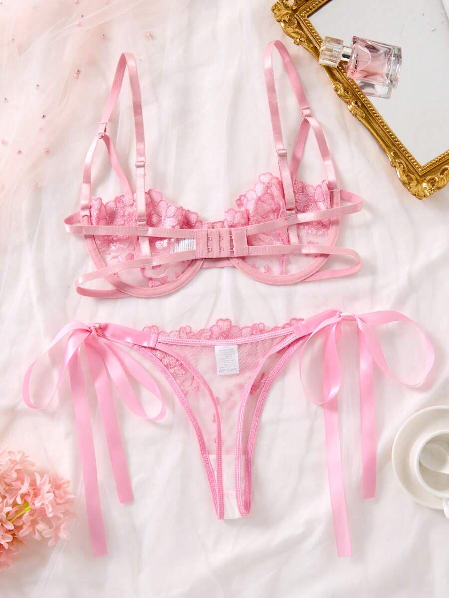 Conjunto de lencería de encaje floral rosa visto desde arriba sobre una superficie blanca.