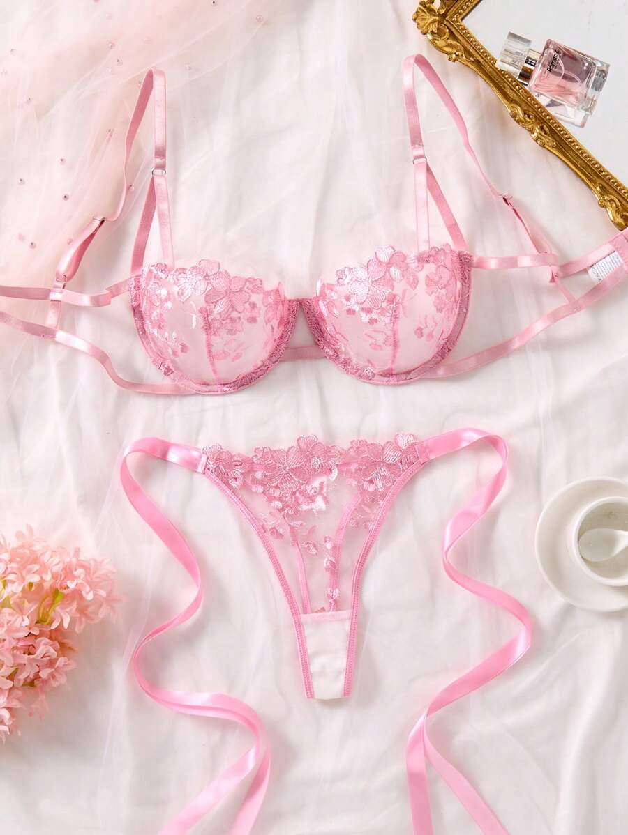 Conjunto de lencería de encaje floral rosa visto desde arriba sobre una superficie blanca.