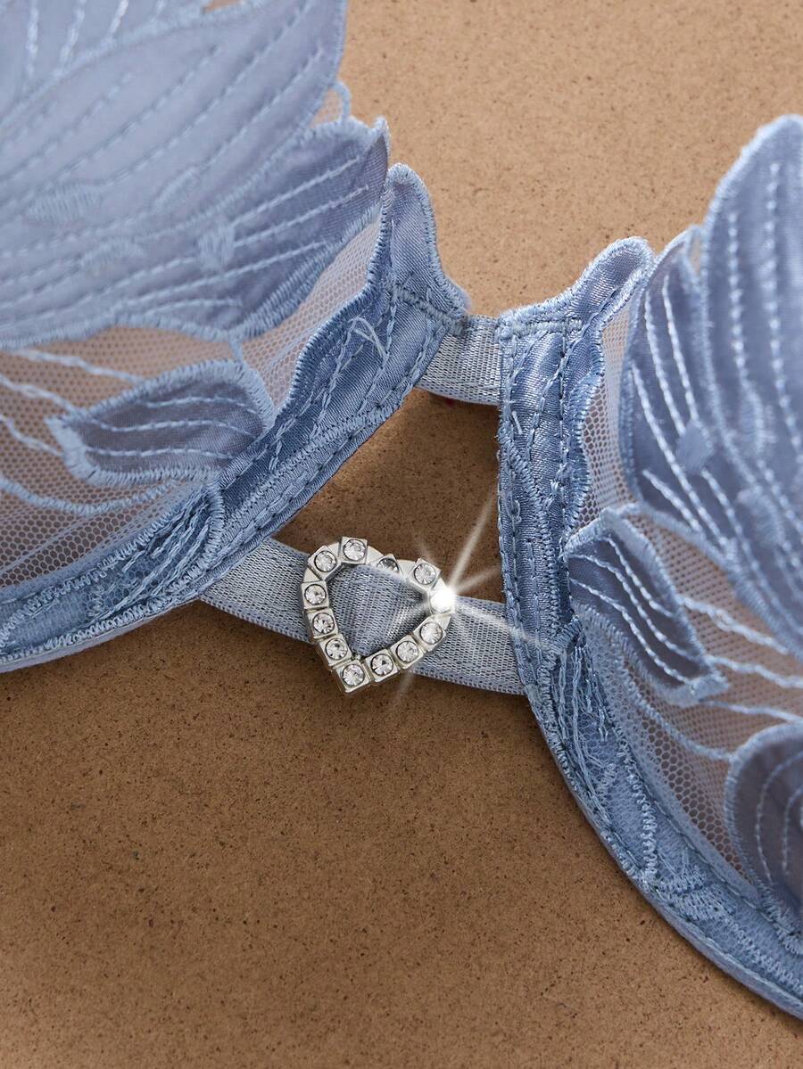 Conjunto de lencería azul cielo con bordado floral sobre un fondo de seda.