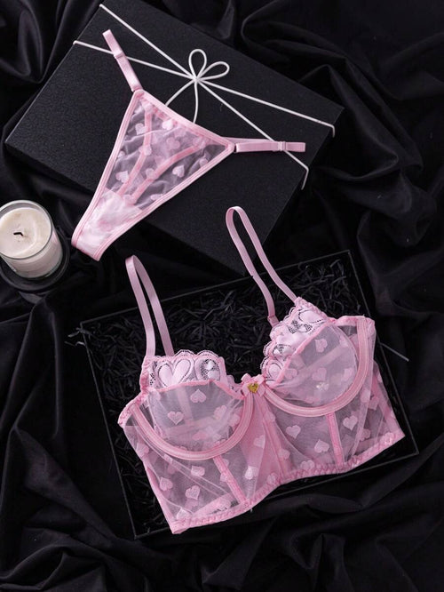 Conjunto de lencería rosa con estampado de corazones sobre un fondo negro satinado.