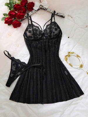 Conjunto de lencería babydoll negro de encaje y tul sobre una cama blanca con rosas rojas.