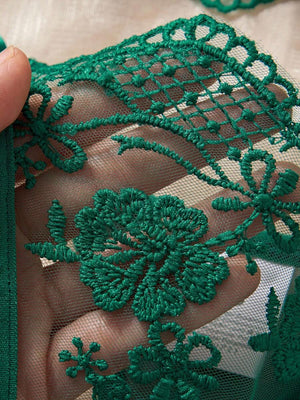 Lencería romántica verde oscuro con encaje y accesorios decorativos sobre tela satinada.