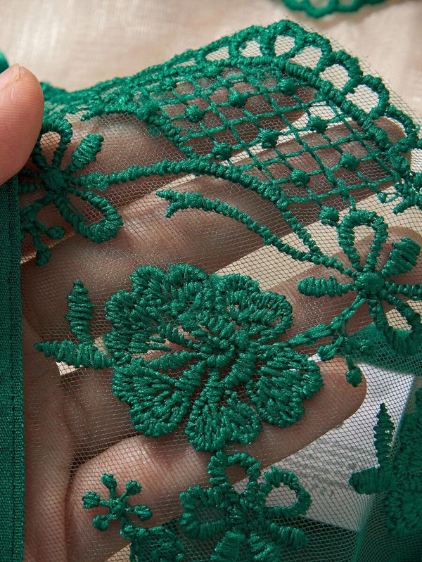 Lencería romántica verde oscuro con encaje y accesorios decorativos sobre tela satinada.