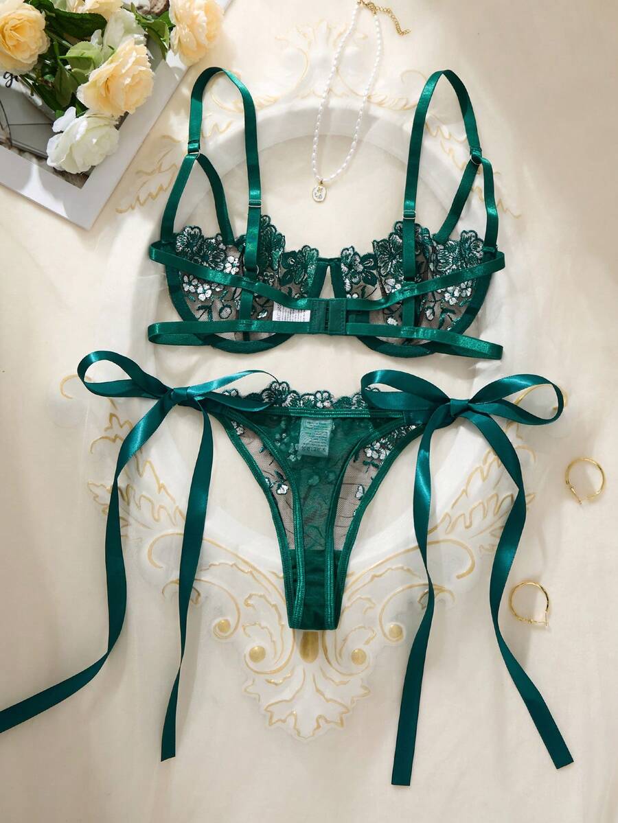 Conjunto de lencería verde esmeralda con bordado floral visto desde arriba sobre una superficie clara.