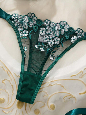 Vista frontal de la tanga de lencería verde con malla transparente, bordado floral y cintas de satén a los lados.