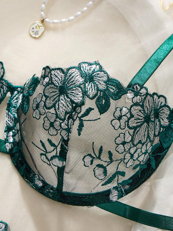 Primer plano del diseño floral bordado en la copa del sujetador de lencería verde esmeralda.