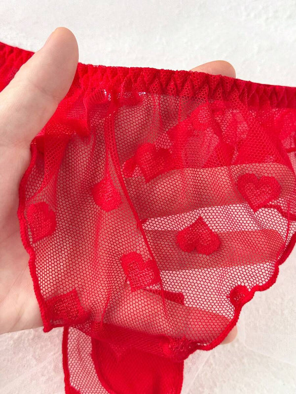 Primer plano de una tanga de lencería roja confeccionada en tul de corazones y borde con volantes.