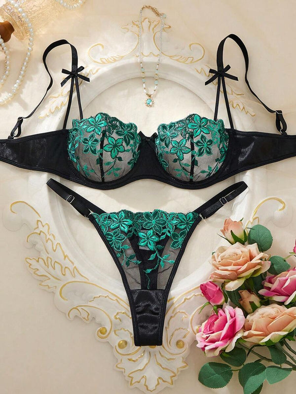 Vista frontal de la tanga negra con bordado floral verde en tul transparente.