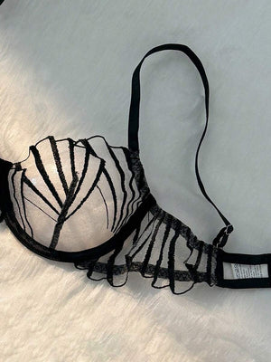 Detalle de la tanga de lencería negra a juego, mostrando el bordado sobre malla transparente.