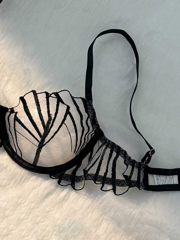 Detalle de la tanga de lencería negra a juego, mostrando el bordado sobre malla transparente.