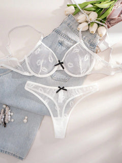 Conjunto de lencería blanco de malla con estampado de labios, mostrado sobre unos jeans y junto a flores.