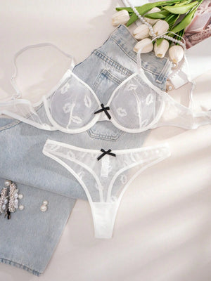 Conjunto de lencería blanco de malla con estampado de labios, mostrado sobre unos jeans y junto a flores.