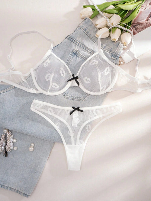Conjunto de lencería blanco de malla con estampado de labios, mostrado sobre unos jeans y junto a flores.