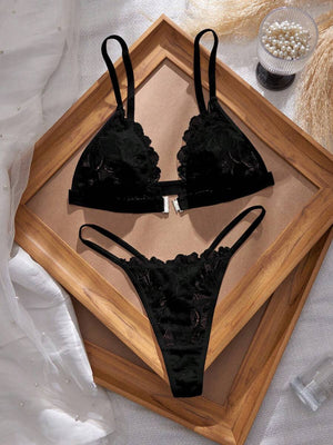 Conjunto de lencería de encaje negro con bralette de cierre frontal y tanga, visto desde arriba sobre un marco de madera.