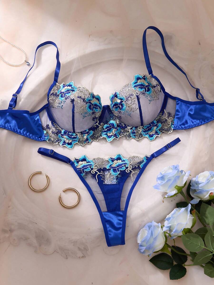 Conjunto de lencería azul zafiro con bordado floral en tonos celestes y plateados, mostrando el brasier y la tanga sobre un fondo claro.