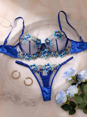 Conjunto de lencería azul zafiro con bordado floral en tonos celestes y plateados, mostrando el brasier y la tanga sobre un fondo claro.