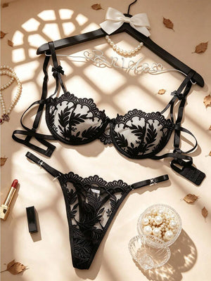 Conjunto de lencería negro con bordado floral colgado en un gancho.