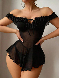 Mujer modelando un babydoll negro de malla transparente con hombros descubiertos y volantes en el escote.