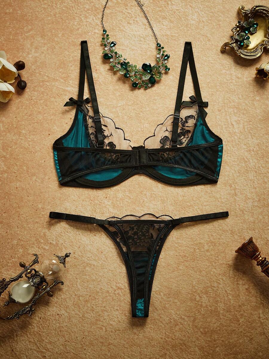 Conjunto de lencería verde esmeralda y negro con bordado floral, visto desde arriba con accesorios decorativos.