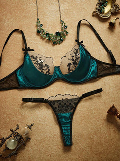 Conjunto de lencería verde esmeralda y negro con bordado floral, visto desde arriba con accesorios decorativos.