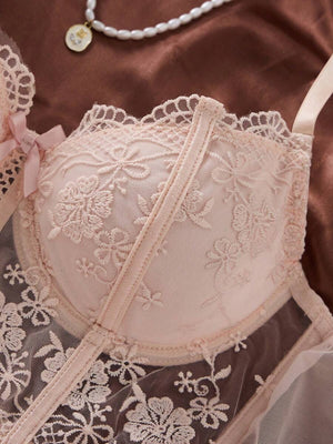 Tanga de lencería rosa pálido con encaje floral transparente, junto a un ramo de rosas.