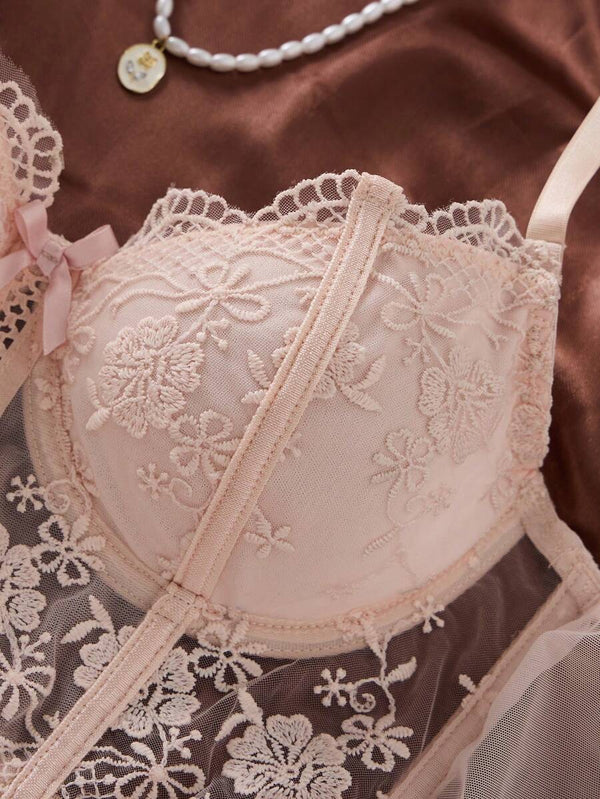 Tanga de lencería rosa pálido con encaje floral transparente, junto a un ramo de rosas.
