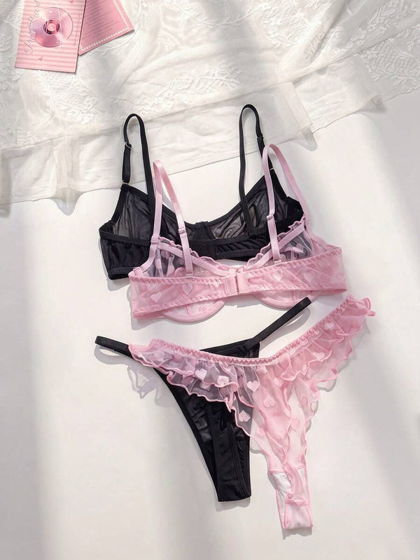 Detalle del sujetador de lencería rosa con estampado de corazones y volantes junto a un sujetador negro de malla.