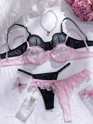 Vista de cerca de la tanga de lencería rosa con malla transparente, estampado de corazones y borde con volantes.