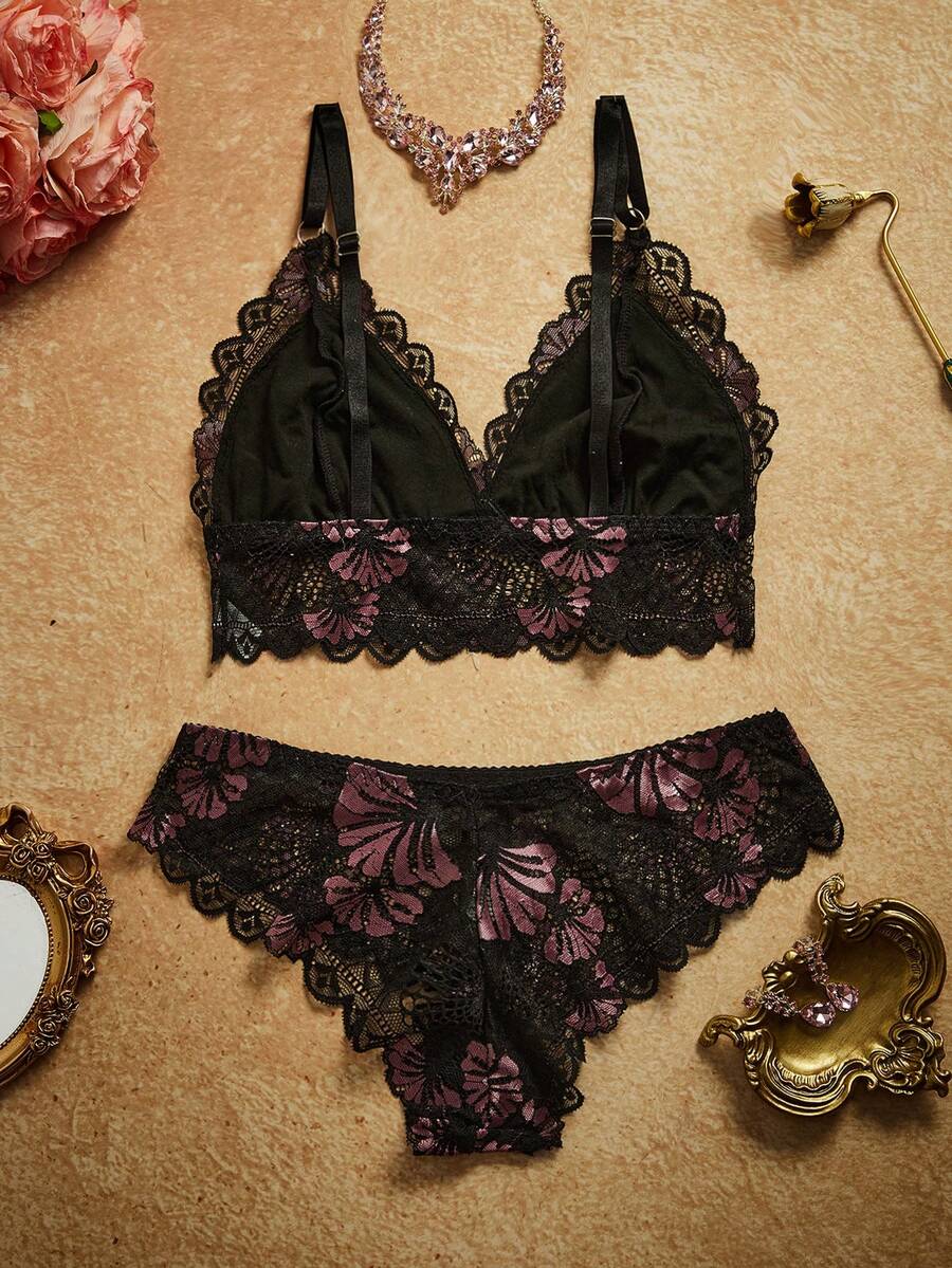 Conjunto de lencería de encaje negro con flores lilas en vista superior sobre un fondo neutro.