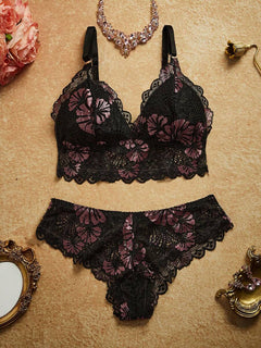 Conjunto de lencería de encaje negro con flores lilas en vista superior sobre un fondo neutro.