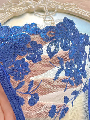 Tanga a juego con el conjunto de lencería, presentando bordados florales y tiras de satén azul.