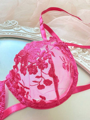 Tanga de lencería rosa fucsia con bordado floral y cintas de satén decorativas.