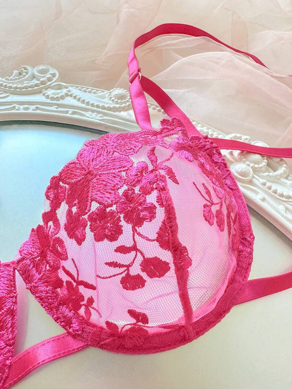 Tanga de lencería rosa fucsia con bordado floral y cintas de satén decorativas.