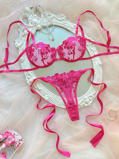 Conjunto de lencería rosa fucsia con bordado floral sobre un espejo de marco blanco.